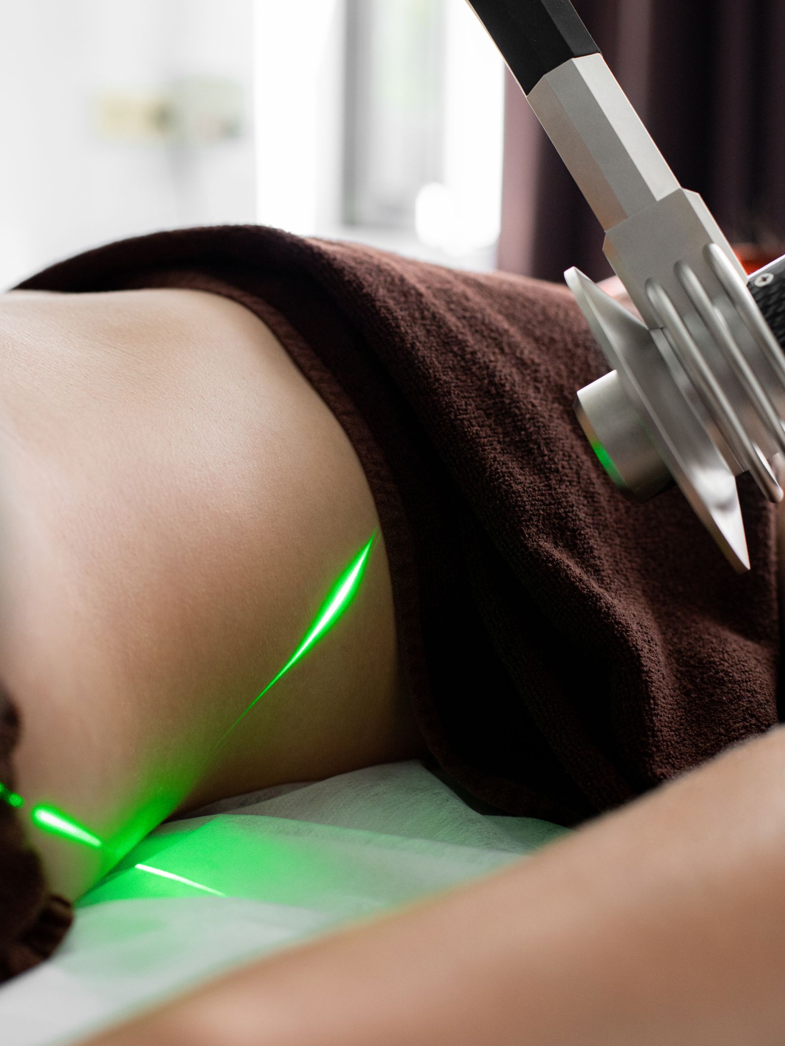 A clinical laser casting precise green light across skin during a treatment in a darkened room